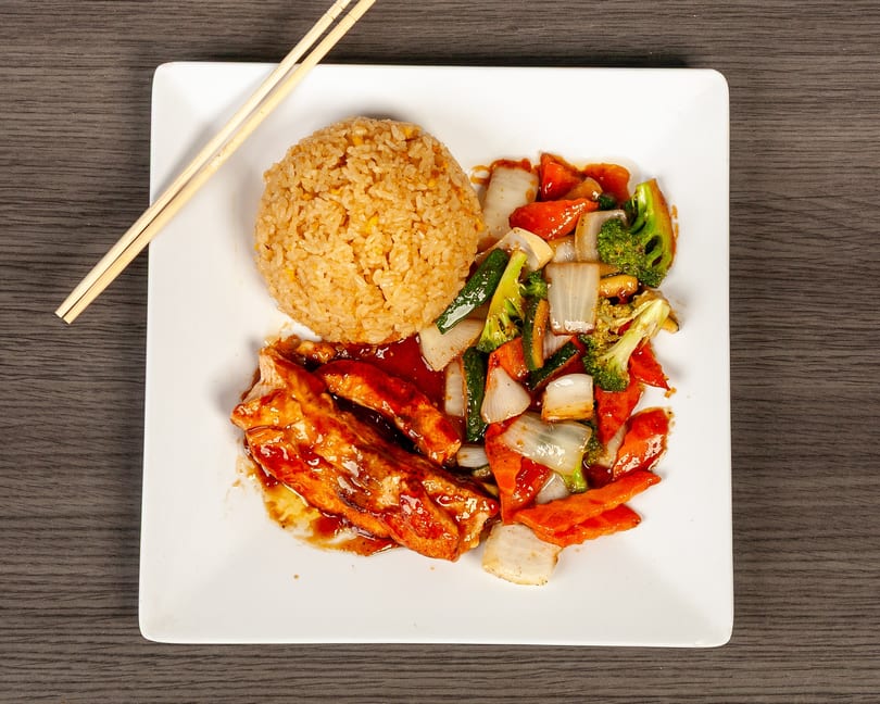 Teriyaki chicken with fried rice and stir-fried vegetables on a white plate with chopsticks.