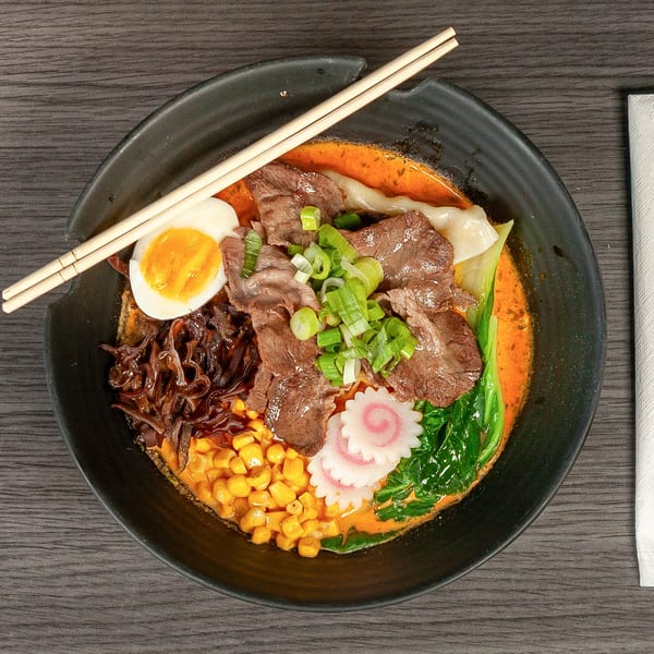 Overhead view of a ramen bowl with beef, egg, corn, scallions, and narutomaki.