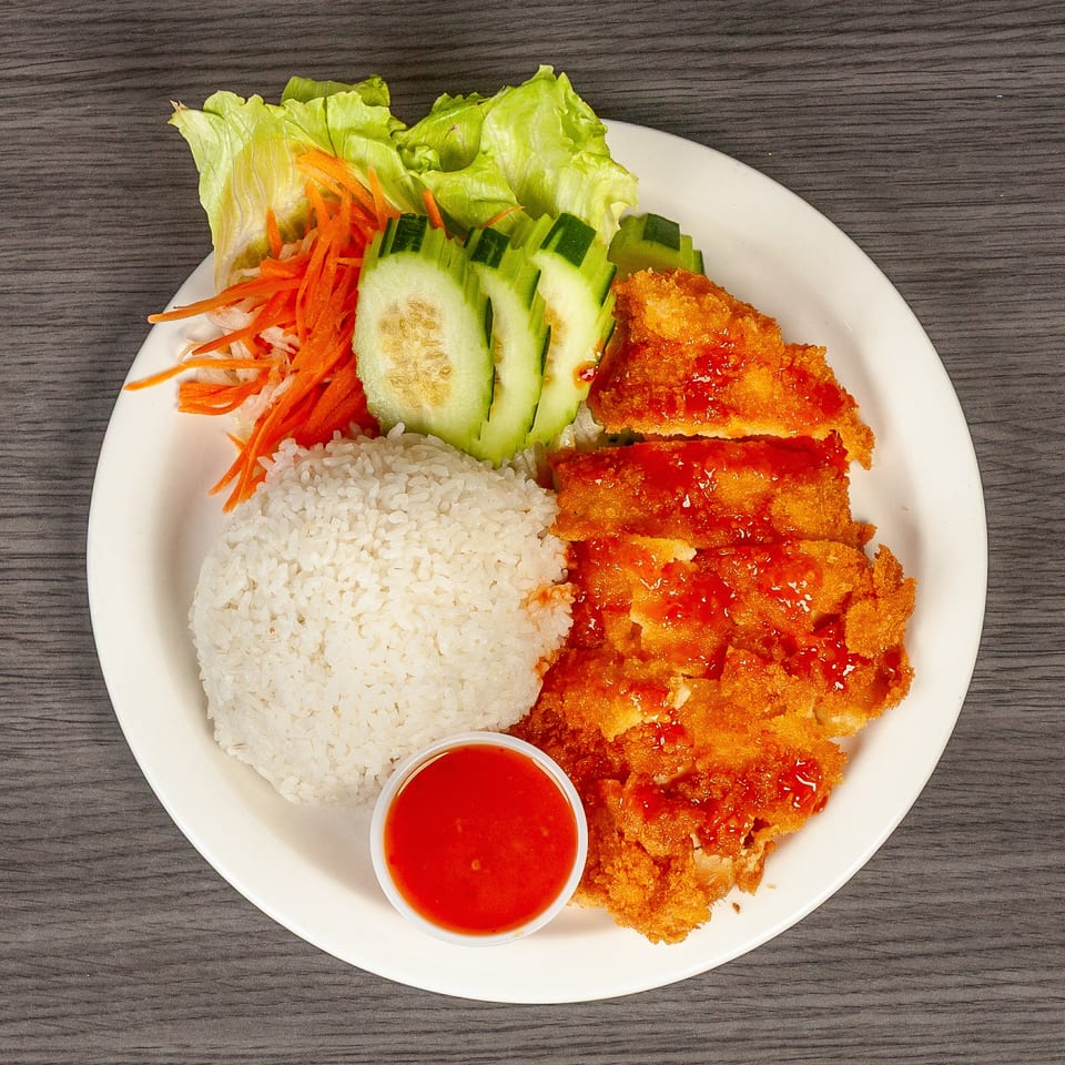 Crispy fried chicken with sweet chili sauce, white rice, lettuce, shredded carrots, and cucumber slices.