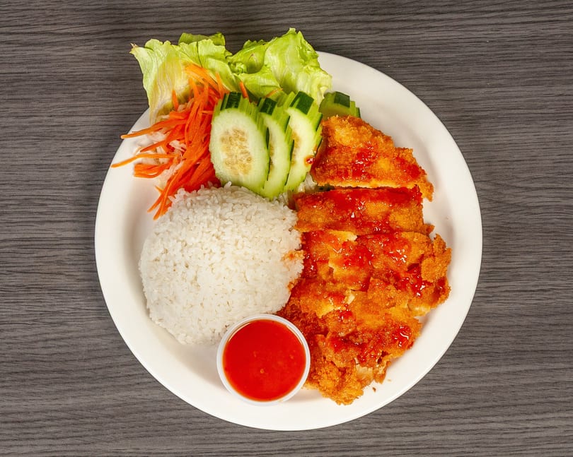 Crispy fried chicken with sweet chili sauce, white rice, lettuce, shredded carrots, and cucumber slices.