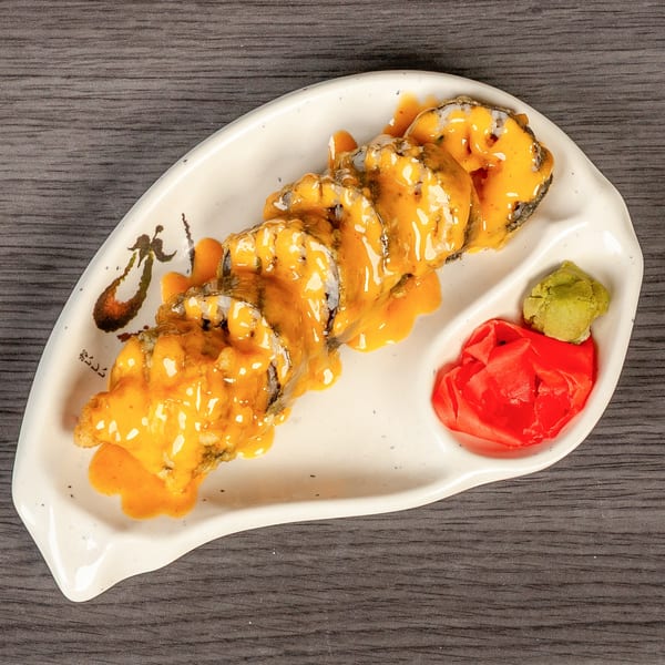 Sushi rolls with orange sauce, wasabi, and pickled ginger on a white plate.
