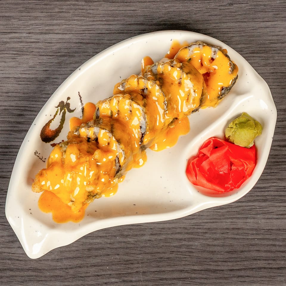 Sushi rolls with orange sauce, wasabi, and pickled ginger on a white plate.