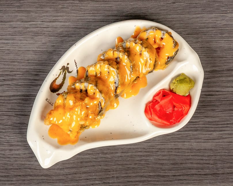 Sushi rolls with orange sauce, wasabi, and pickled ginger on a white plate.