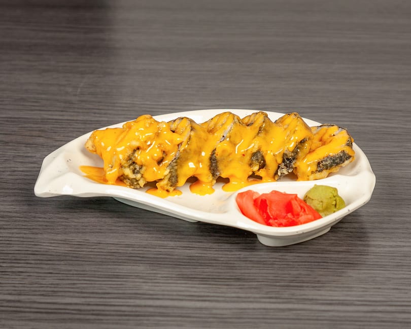A white plate of sushi rolls topped with orange sauce, with ginger and wasabi on the side.