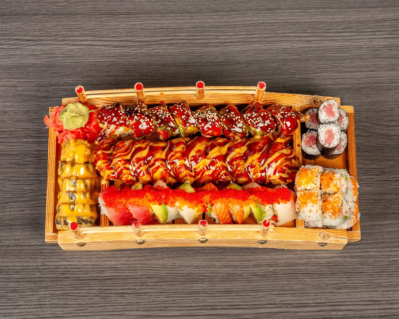 A large wooden boat filled with various sushi rolls, including tuna, salmon, and eel.