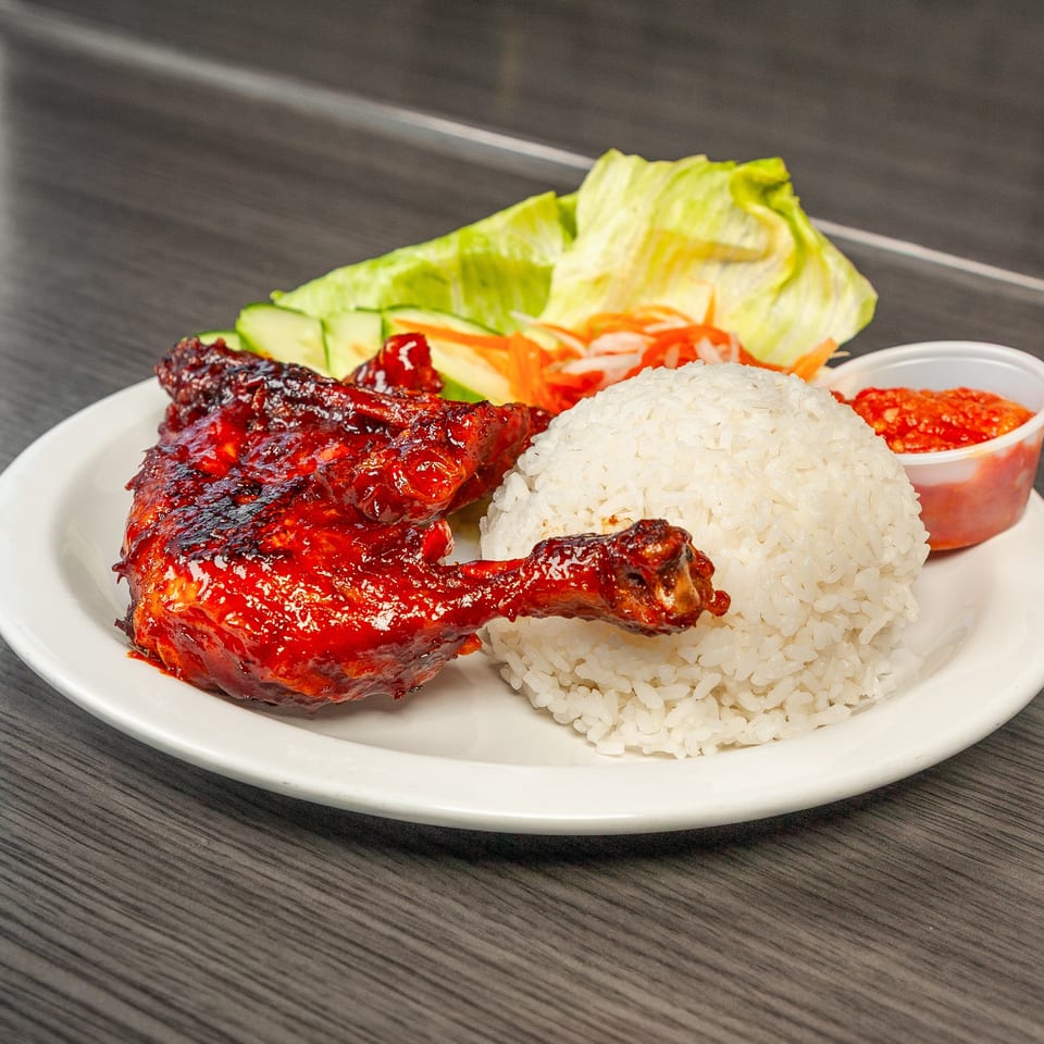 Grilled chicken leg and thigh with white rice, lettuce, cucumber, pickled carrots, and chili sauce.