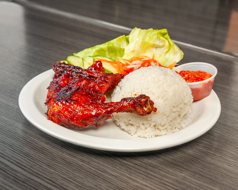 Grilled chicken leg and thigh with white rice, lettuce, cucumber, pickled carrots, and chili sauce.