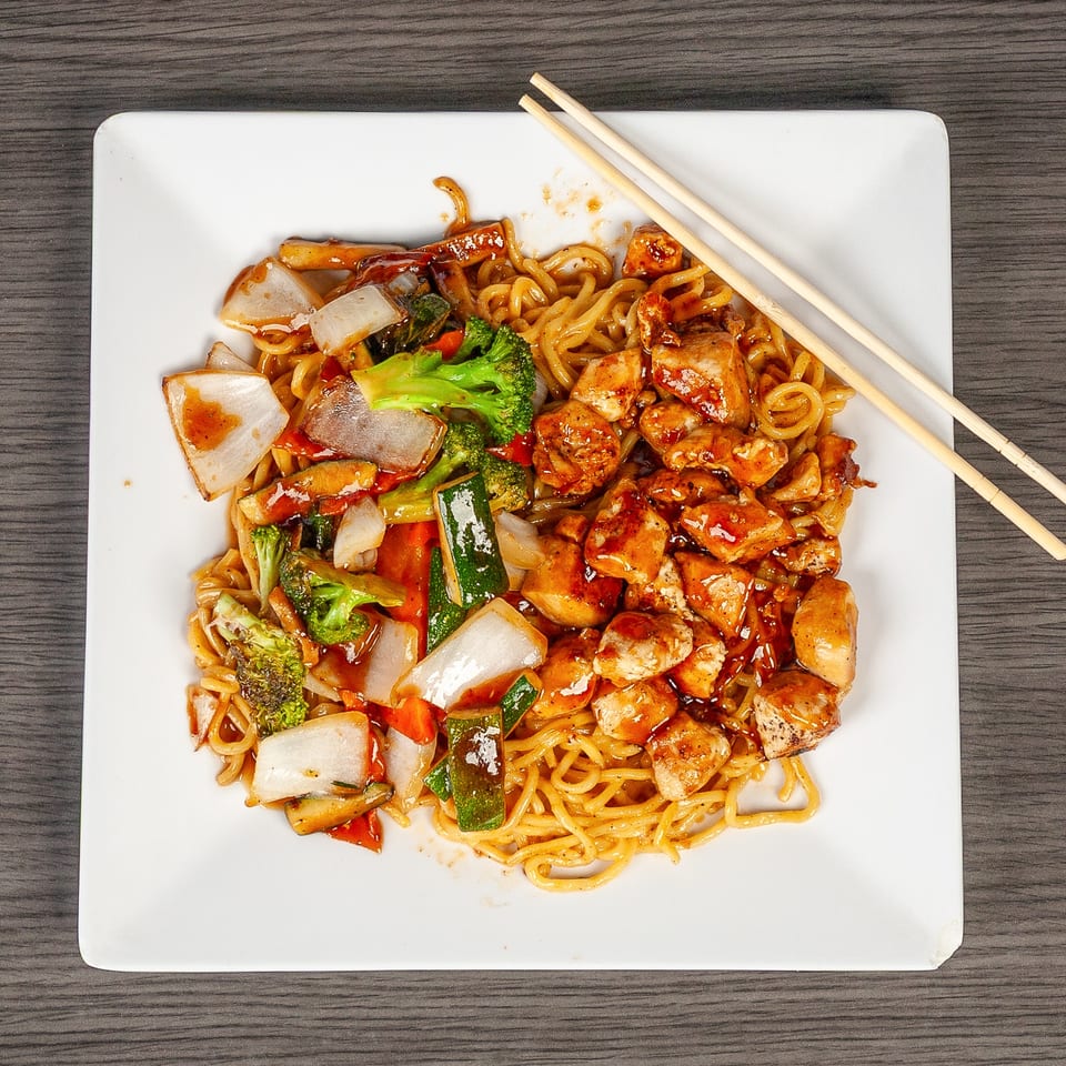 Chicken and vegetable lo mein with chopsticks on a white square plate.