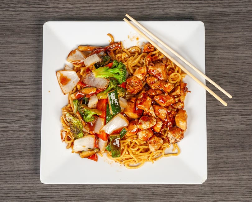Chicken and vegetable lo mein with chopsticks on a white square plate.